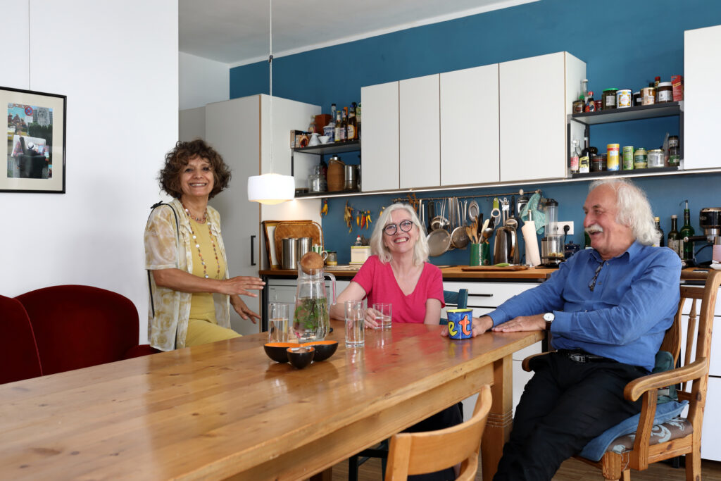 Zwei Frauen und ein Mann sitzen an einem großen Tisch in einer Küche. 